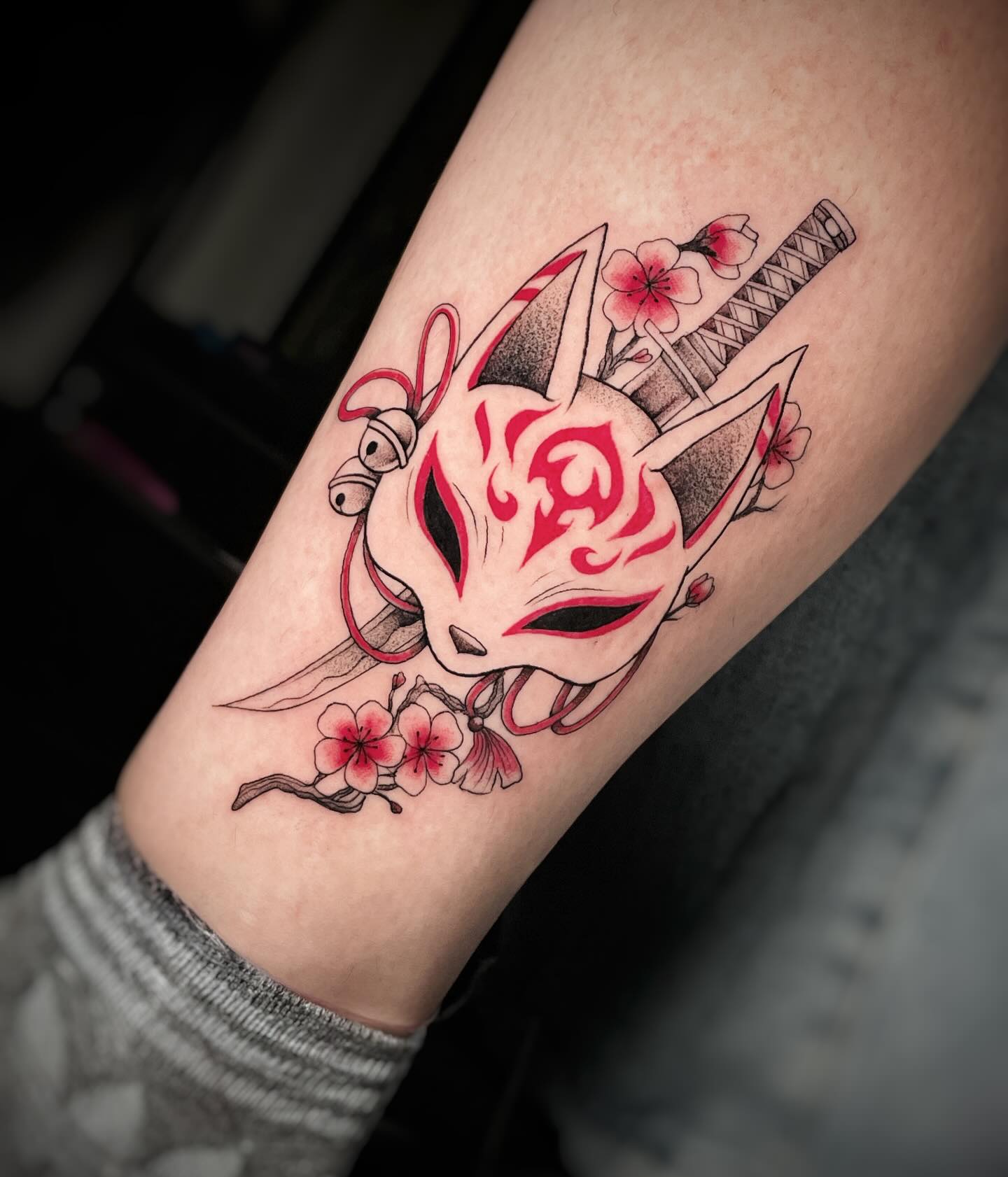 Tatuaje a color de máscara kitsune roja con katana y flores de cerezo en la pantorrilla